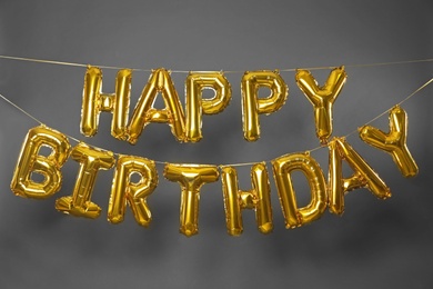 Photo of Phrase HAPPY BIRTHDAY made of golden balloon letters on grey background