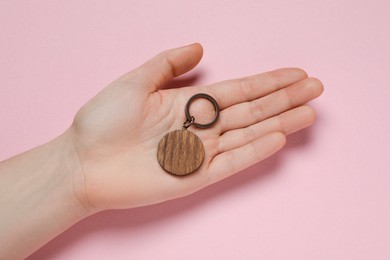 Photo of Woman holding wooden keychain on pale pink background, top view