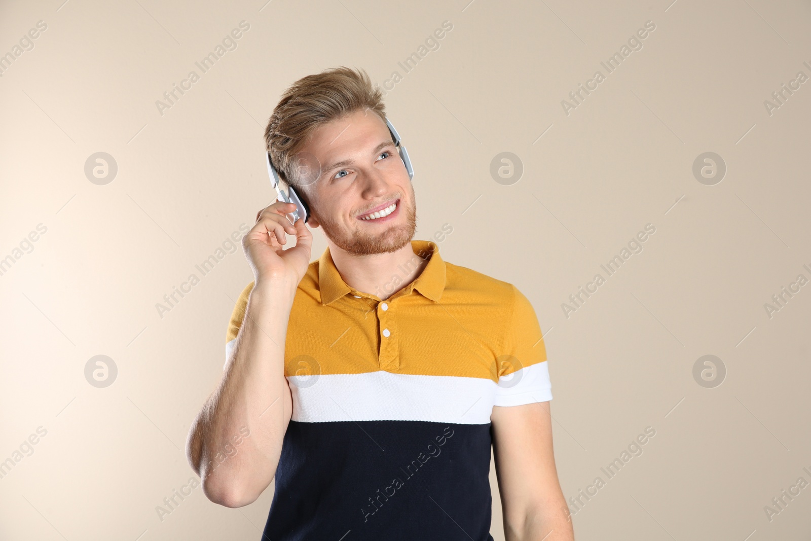 Photo of Handsome young man listening to music with headphones on color background