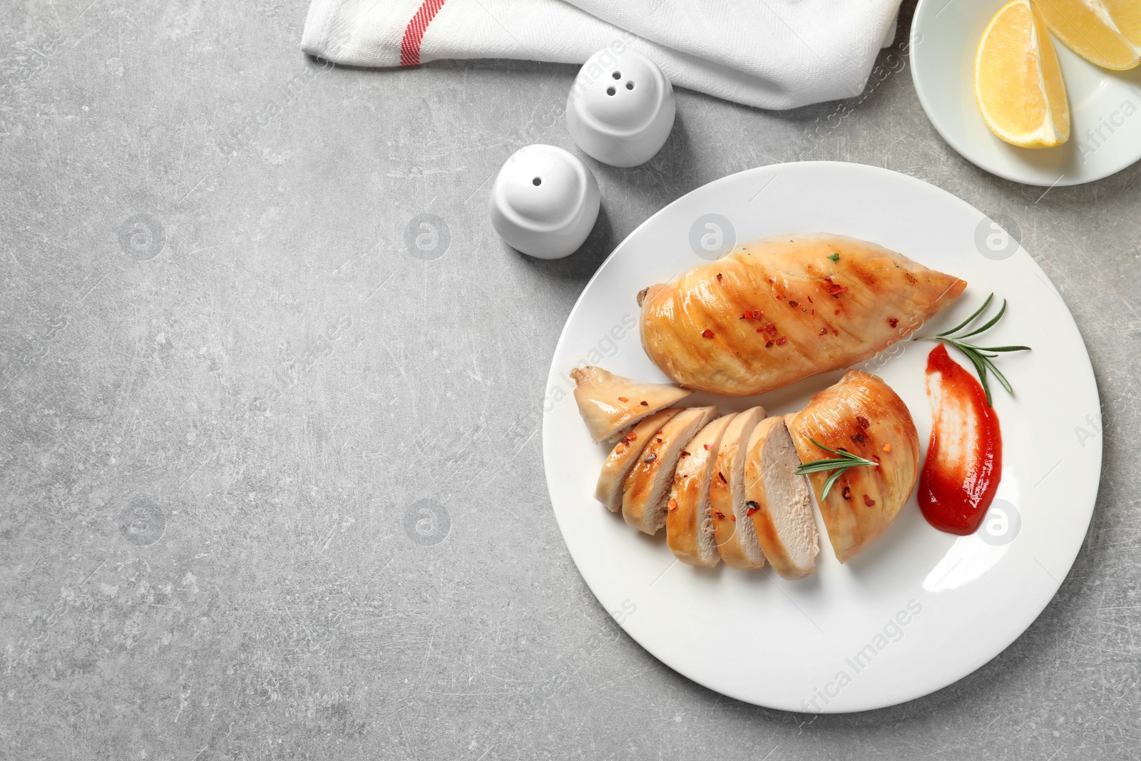 Photo of Fried chicken breasts served with sauce and lemon on grey table, top view. Space for text