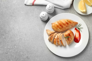 Fried chicken breasts served with sauce and lemon on grey table, top view. Space for text