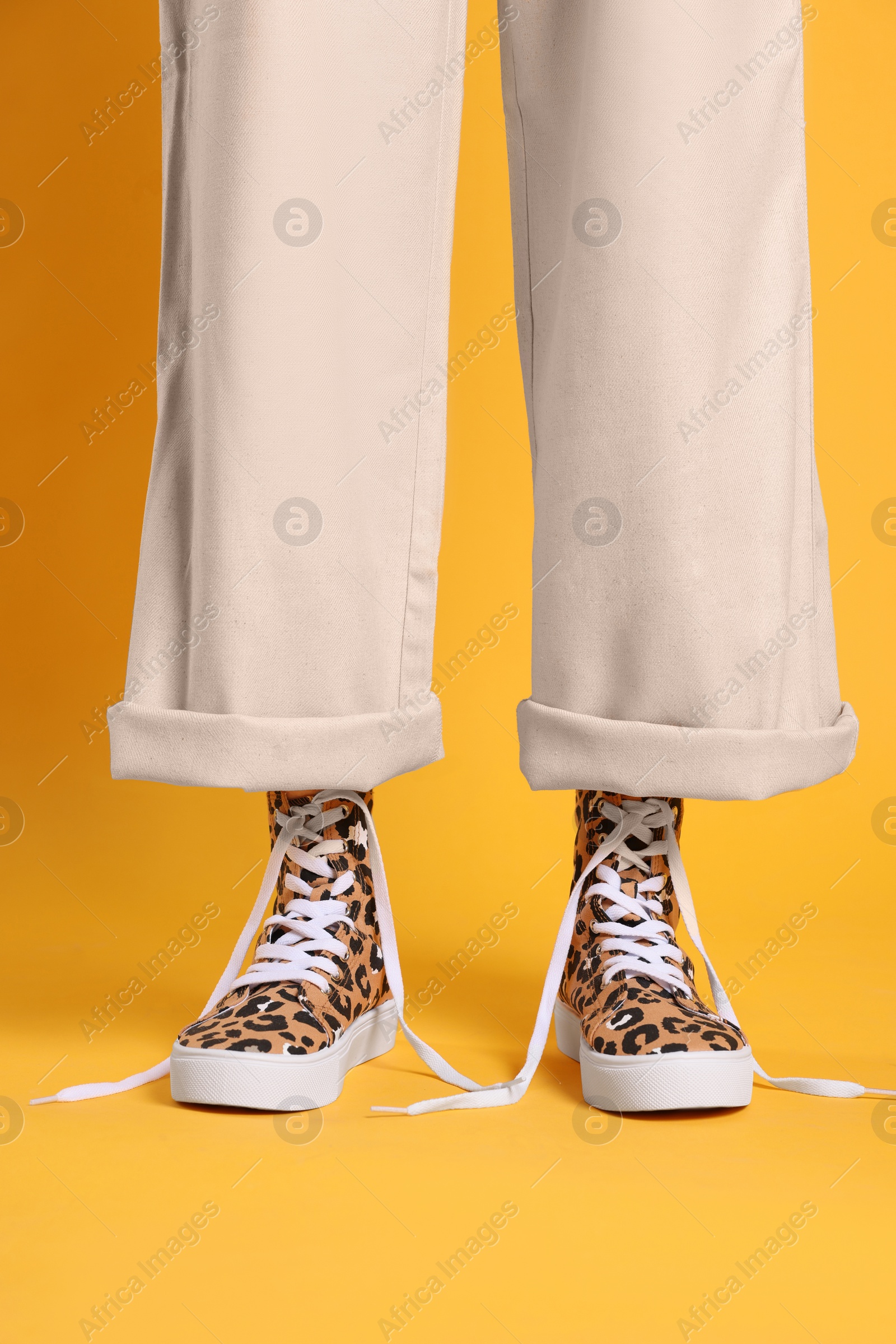 Photo of Woman wearing classic old school sneakers with leopard print on orange background, closeup