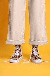 Photo of Woman wearing classic old school sneakers with leopard print on orange background, closeup