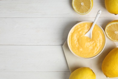 Photo of Delicious lemon curd in bowl on white wooden table, flat lay. Space for text