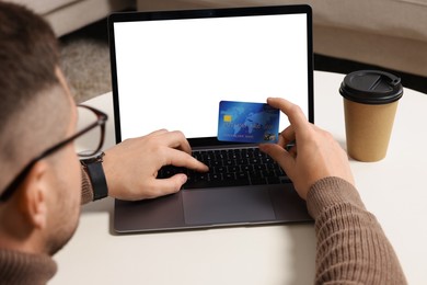 Man with credit card using laptop for online shopping at white table indoors, closeup