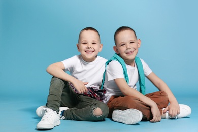 Full length portrait of cute twin brothers sitting on color background