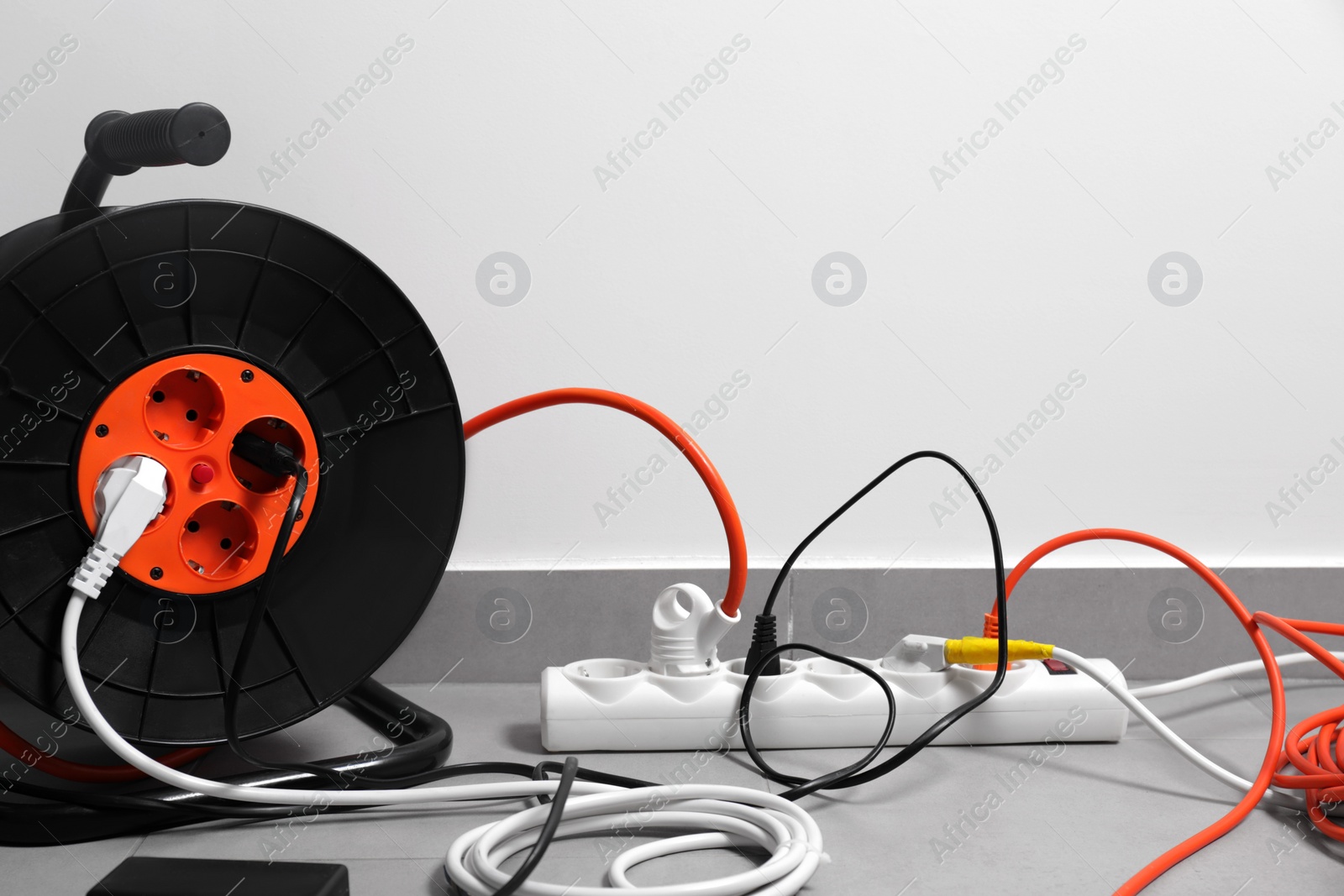 Photo of Extension cord reel plugged into power strip on grey floor indoors, space for text