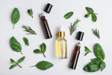 Little bottles of essential oils with different herbs on white background, top view