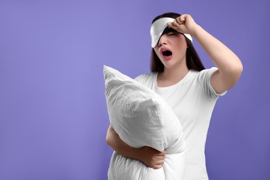 Tired young woman with sleep mask and pillow yawning on purple background, space for text. Insomnia problem