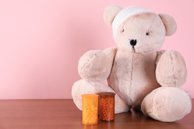 Photo of Toy bear and pills on table against color background, space for text. Children's hospital