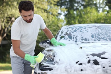 Photo of Man in rubber gloves washing car with sponge outdoors