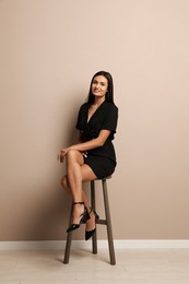 Photo of Beautiful young woman sitting on stool near beige wall