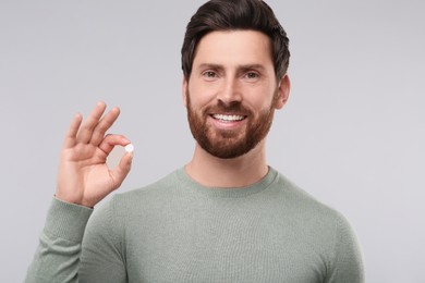 Handsome man with pill on light grey background