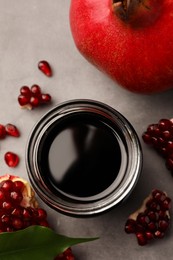 Glass jar of tasty pomegranate sauce and fresh ripe fruit on light grey table, flat lay