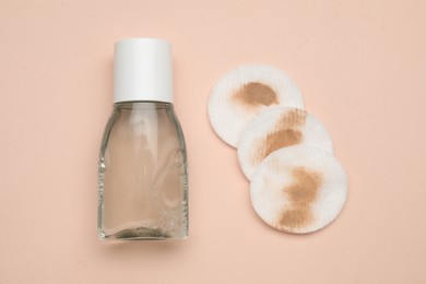 Bottle of makeup remover and dirty cotton pads on beige background, flat lay