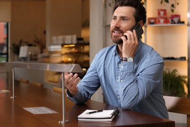 Photo of Handsome man talking on phone at table in cafe