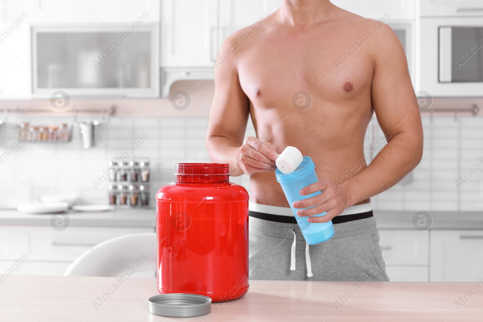 Photo of Young shirtless man preparing protein shake at table in kitchen, closeup. Space for text