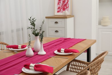 Beautiful table setting and vases with green branches in dining room