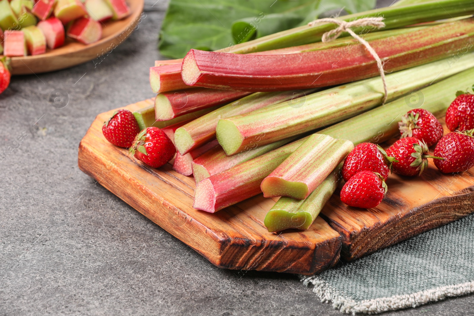 Photo of Fresh ripe rhubarb stalks and strawberries on grey table, closeup