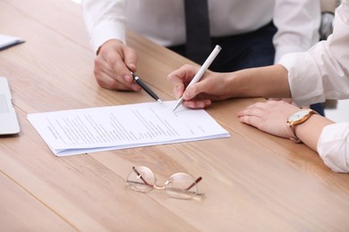 Photo of Businesspeople signing contract at wooden table, closeup