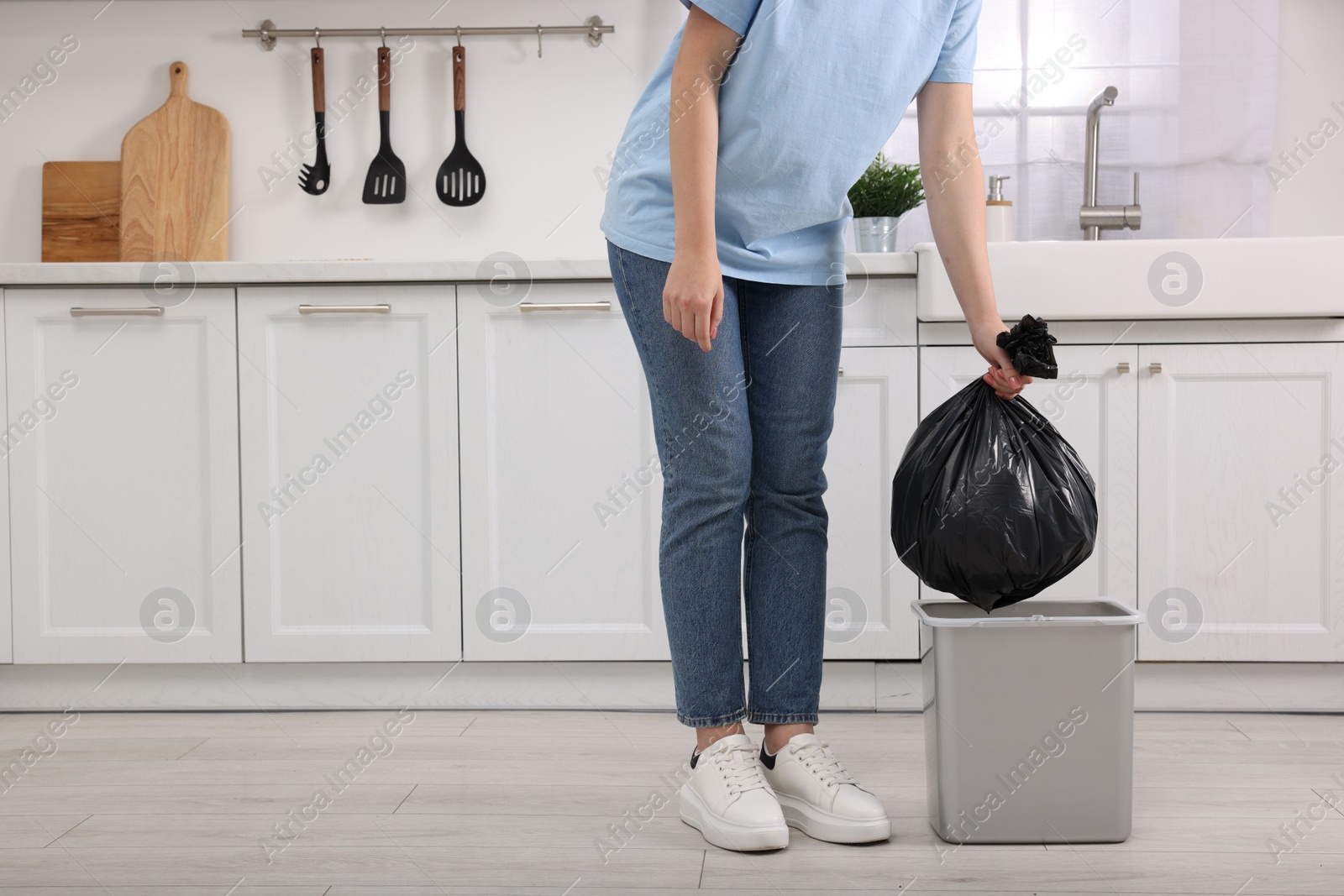 Photo of Woman taking garbage bag out of trash bin in kitchen, closeup. Space for text