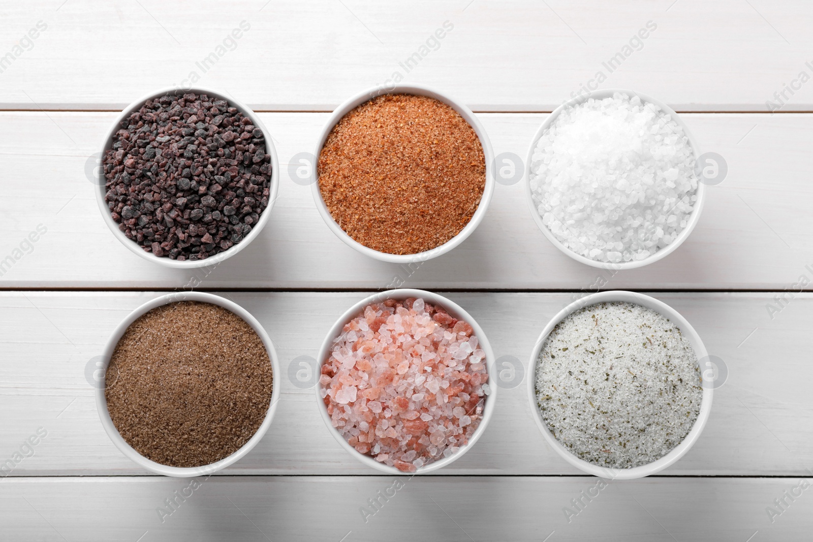 Photo of Different kinds of salt on white wooden table, flat lay