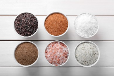 Photo of Different kinds of salt on white wooden table, flat lay