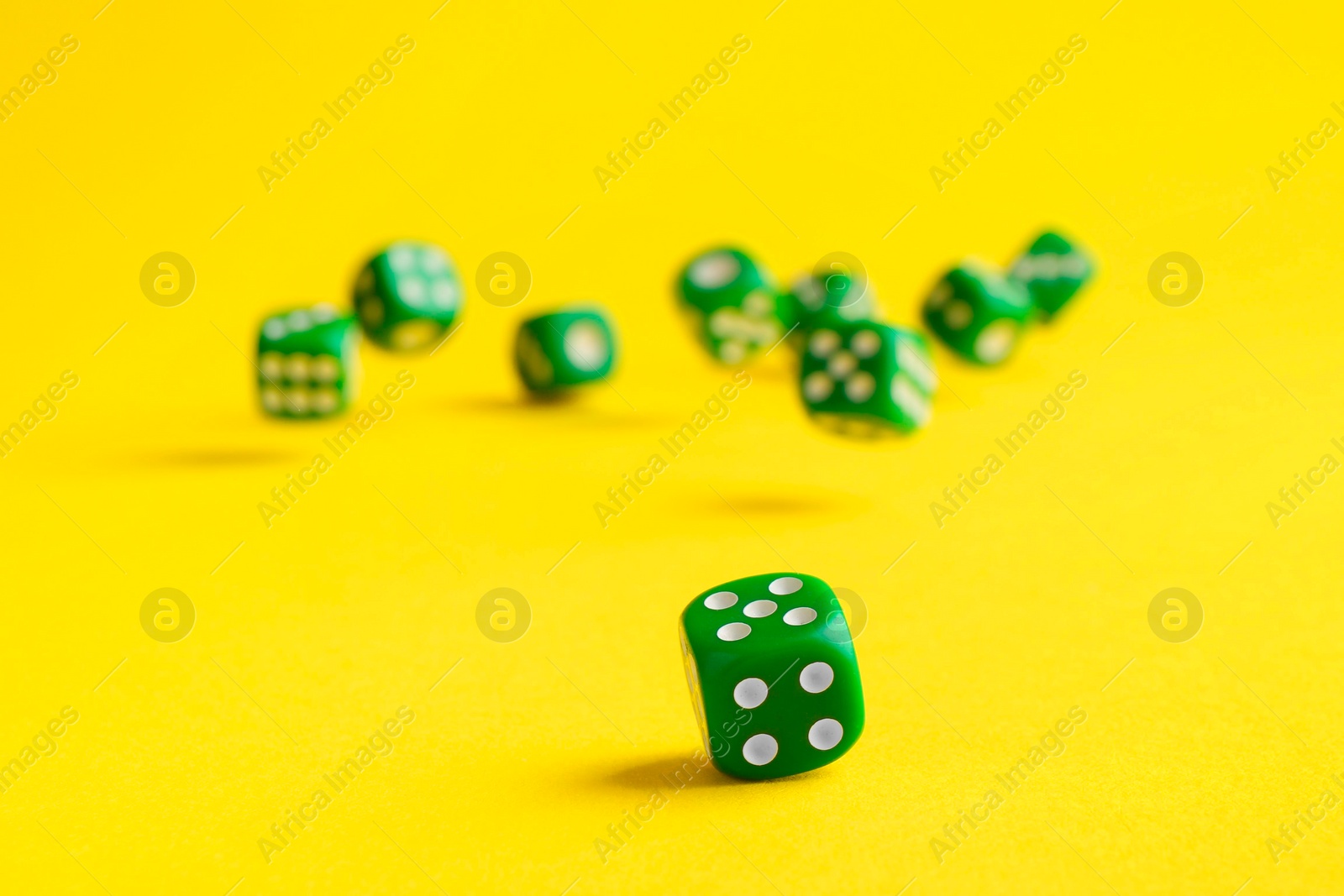 Photo of Many green game dices falling on yellow background