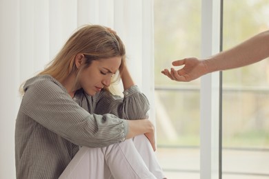 Man offering hand to depressed woman indoors