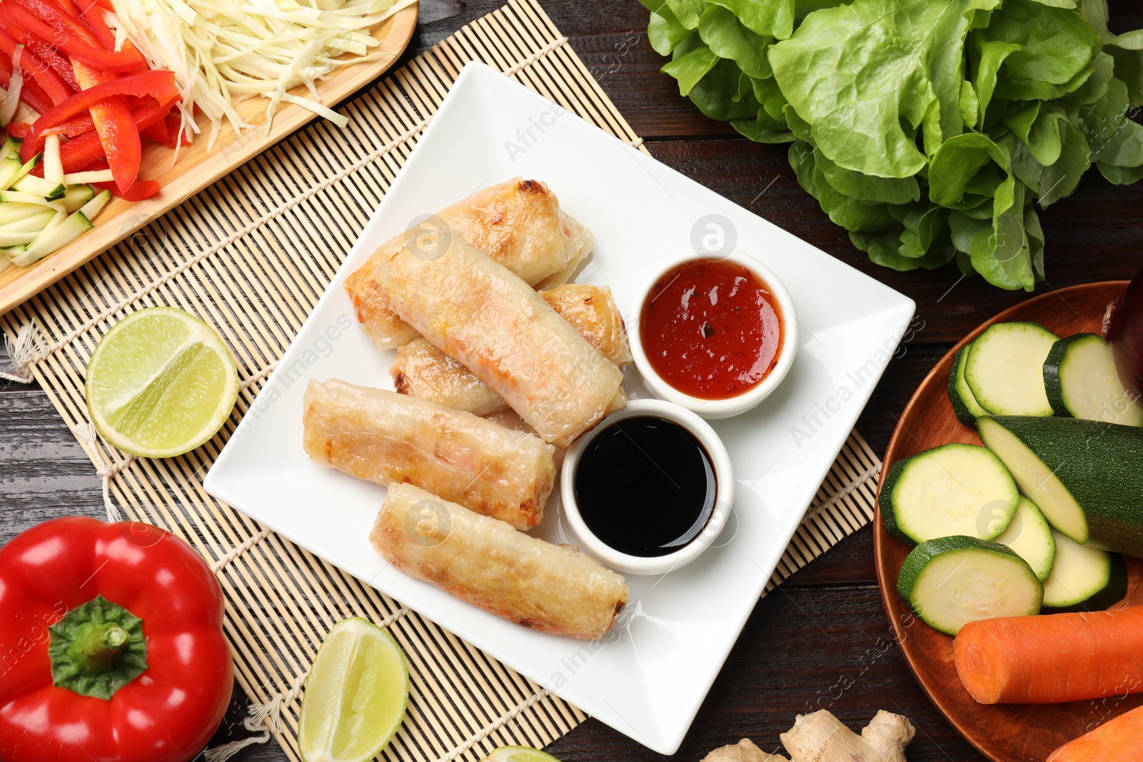 Photo of Tasty fried spring rolls, sauces and fresh products on wooden table, flat lay
