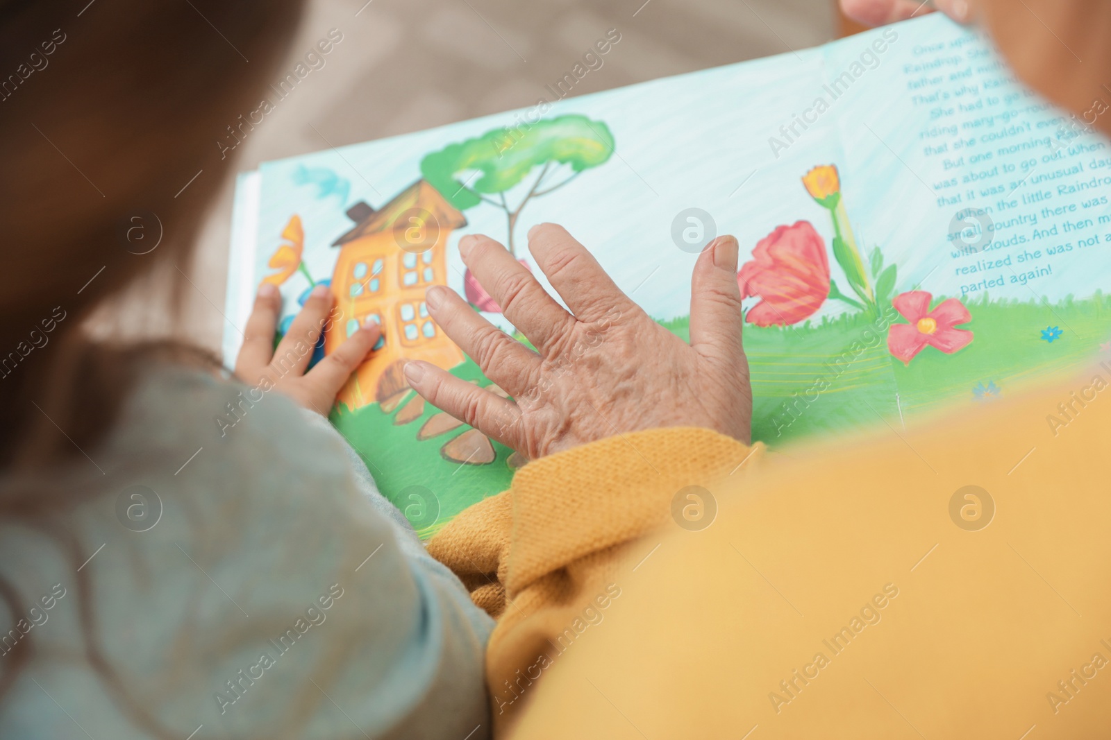 Photo of Cute girl and her grandmother reading book at home, closeup