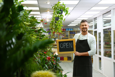 Photo of Male business owner holding OPEN sign in his flower shop