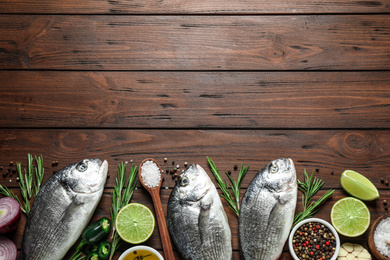 Flat lay composition with raw dorada fish on wooden table, space for text
