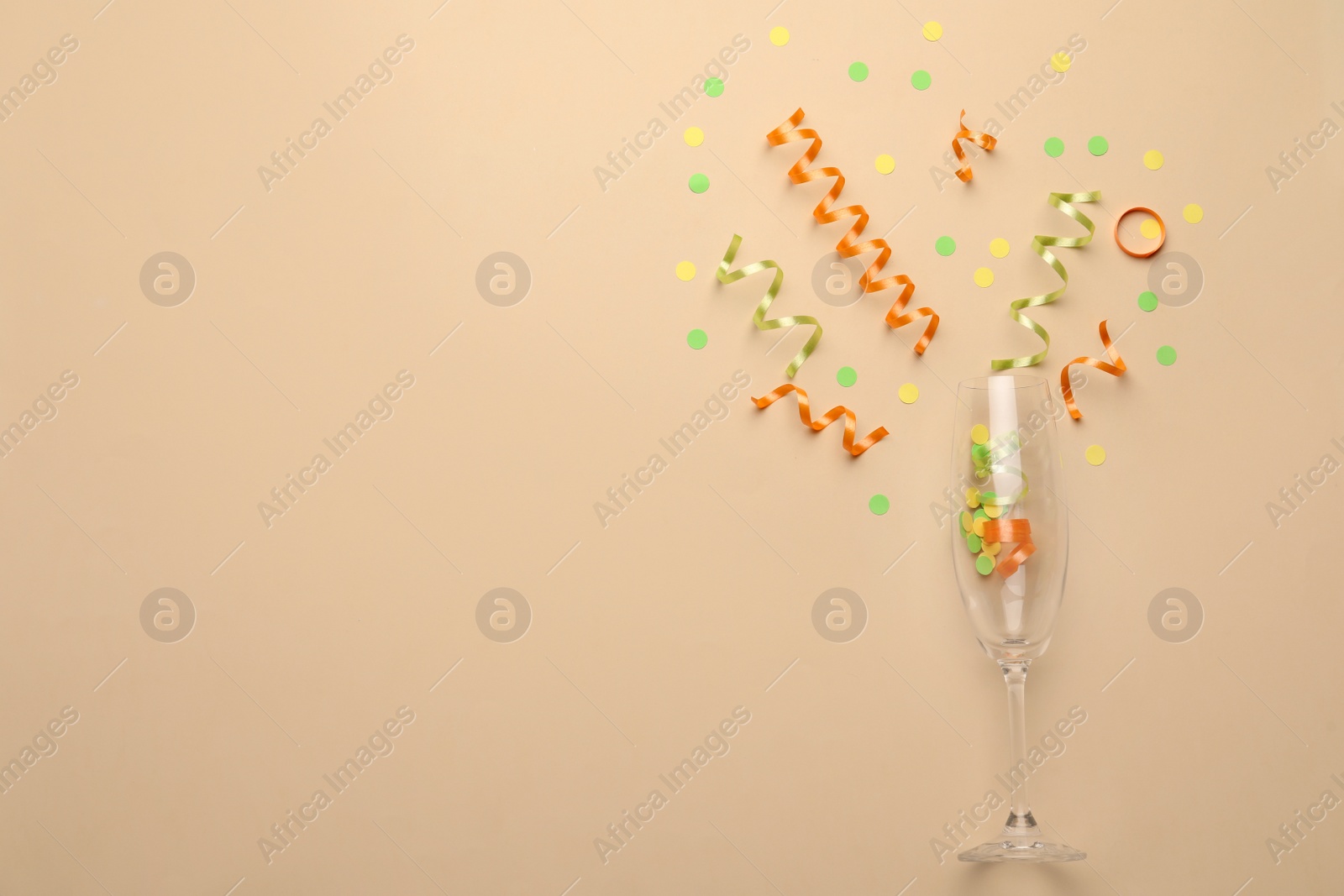 Photo of Glass and shiny confetti on beige background, flat lay. Space for text