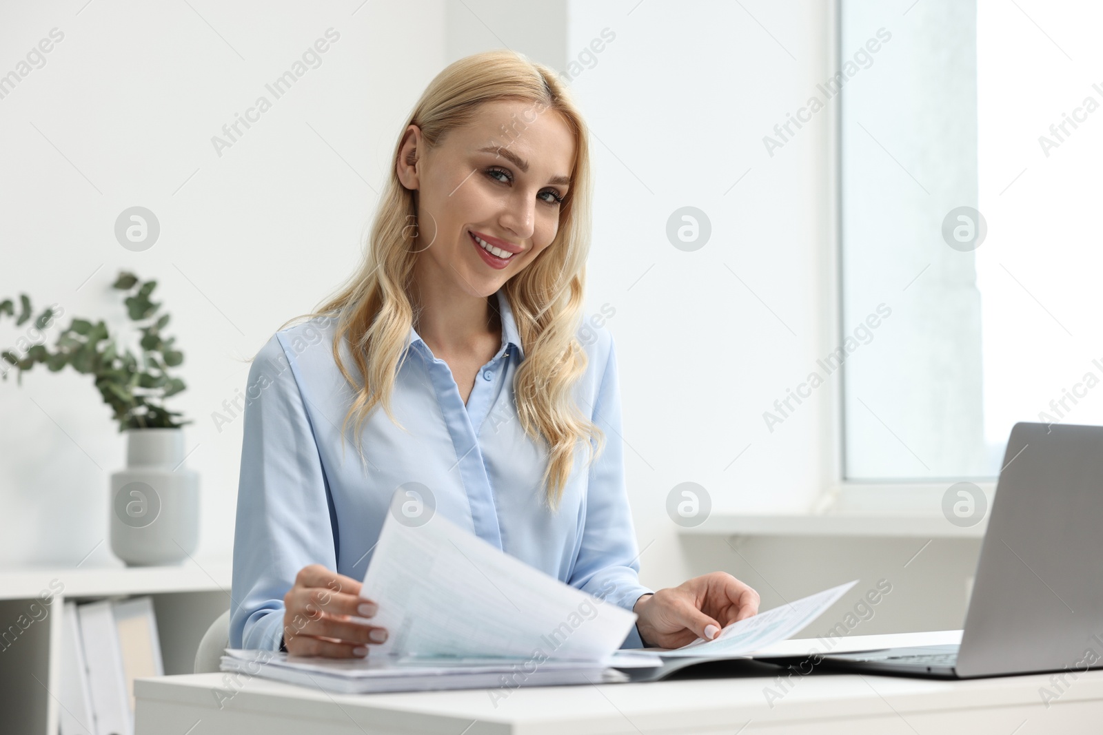 Photo of Happy secretary working with documents at table in office