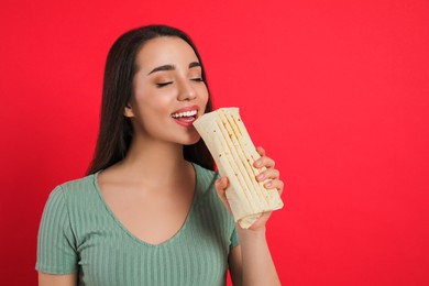 Photo of Young woman eating tasty shawarma on red background. Space for text