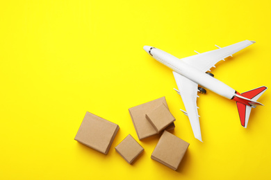 Photo of Top view of toy plane with boxes on yellow background, space for text. Logistics and wholesale concept