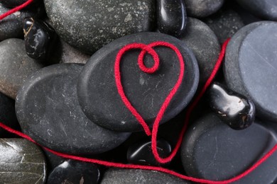 Photo of Heart made of thread on pebble stones, top view