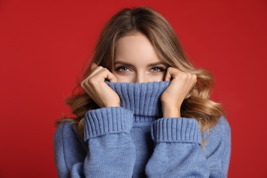 Happy young woman wearing warm sweater on red background. Christmas celebration