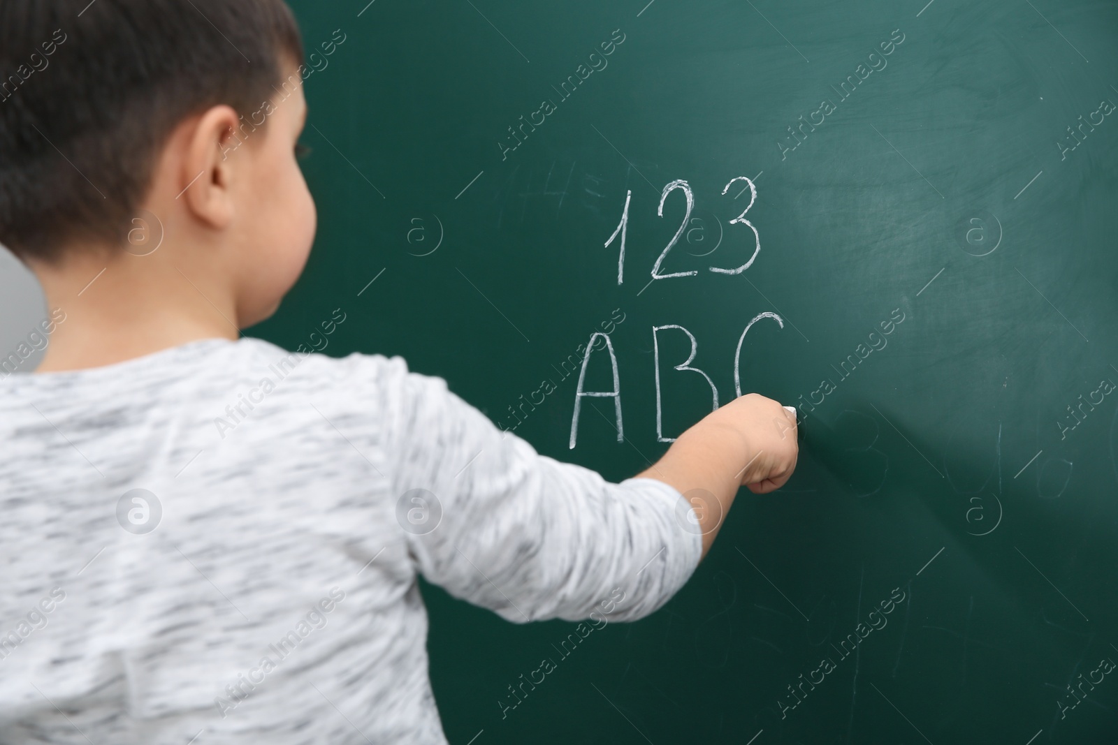 Photo of Little child writing letters and numbers on chalkboard