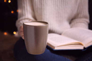 Woman with cup of coffee reading book at home, closeup