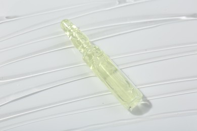 Photo of Skincare ampoule on white surface covered with gel, closeup