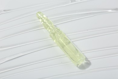 Skincare ampoule on white surface covered with gel, closeup