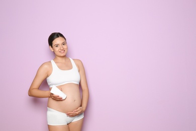 Photo of Pregnant woman holding body cream on color background with space for text