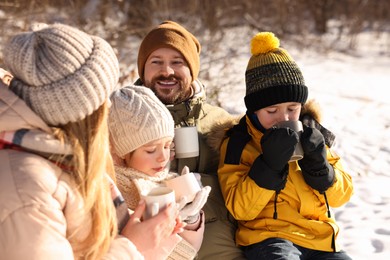 Photo of Happy family warming themselves with hot tea outdoors on snowy day