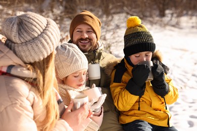 Happy family warming themselves with hot tea outdoors on snowy day