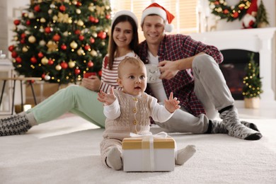 Photo of Happy family in room decorated for Christmas, focus on baby with gift box