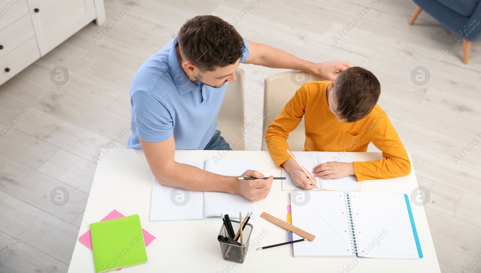 Photo of Dad helping his son with homework in room, above view