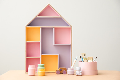 Photo of Composition with house shaped shelf and jars of paints on table. Interior element