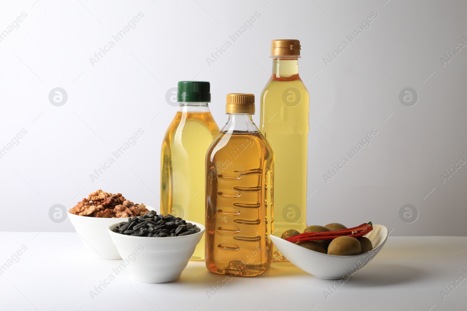 Photo of Bottles of different cooking oils, sunflower seeds, walnuts and olives on white background